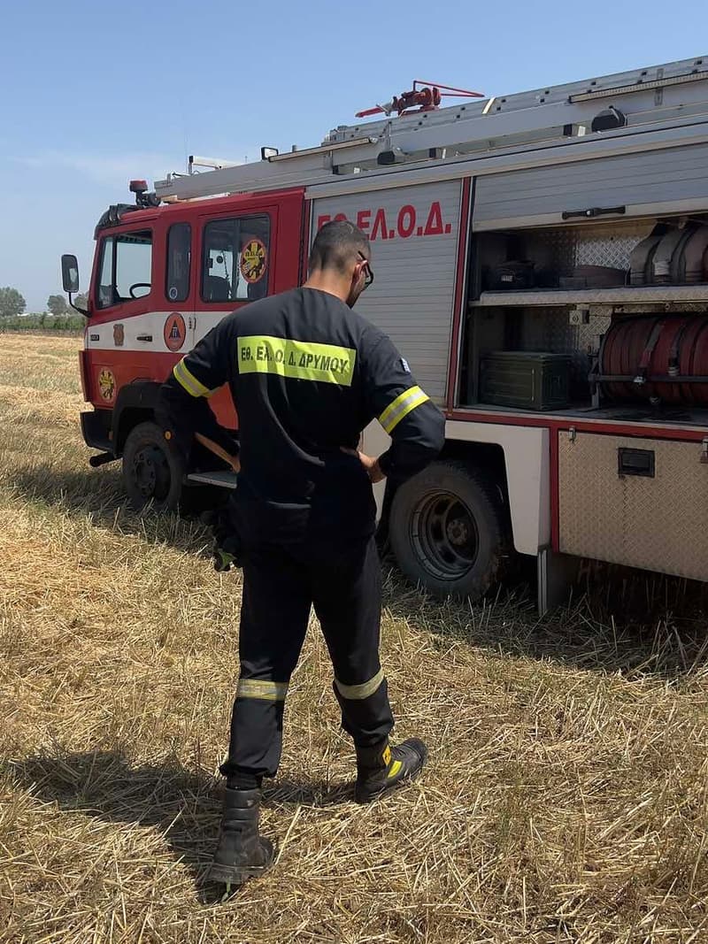 Εθελοντής δίπλα στο πυροσβεστικό όχημα σε ξερό χωράφι